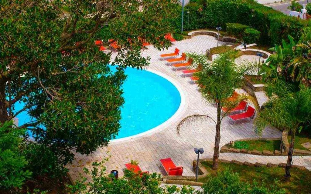 Piscina circolare con lettini arancioni e palme in giardino curato