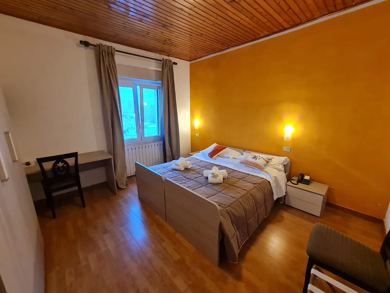 Camera matrimoniale con parete gialla, soffitto in legno e finestra con vista