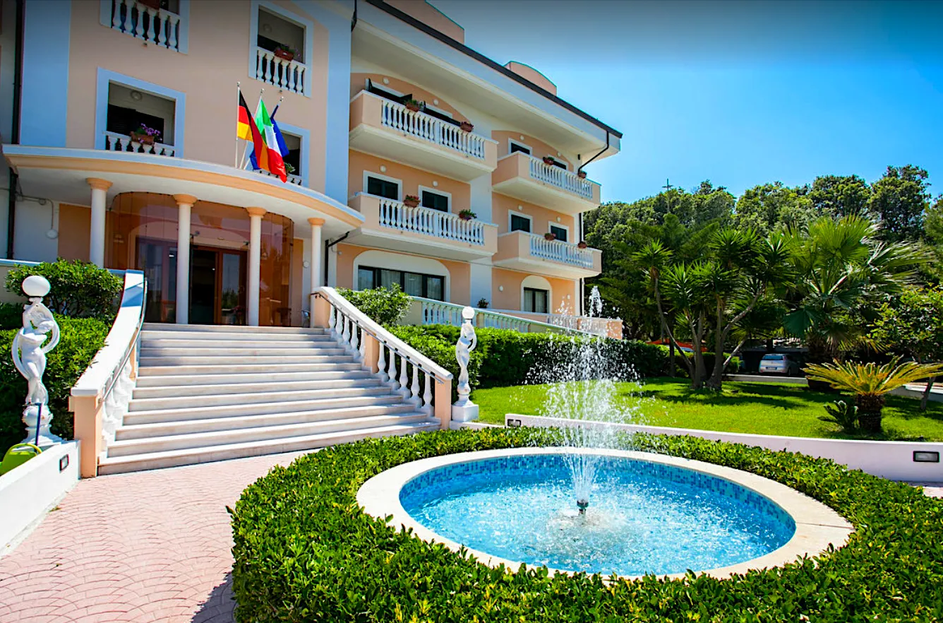 Facciata dell'hotel con scalinata, colonne, bandiere e fontana nel giardino