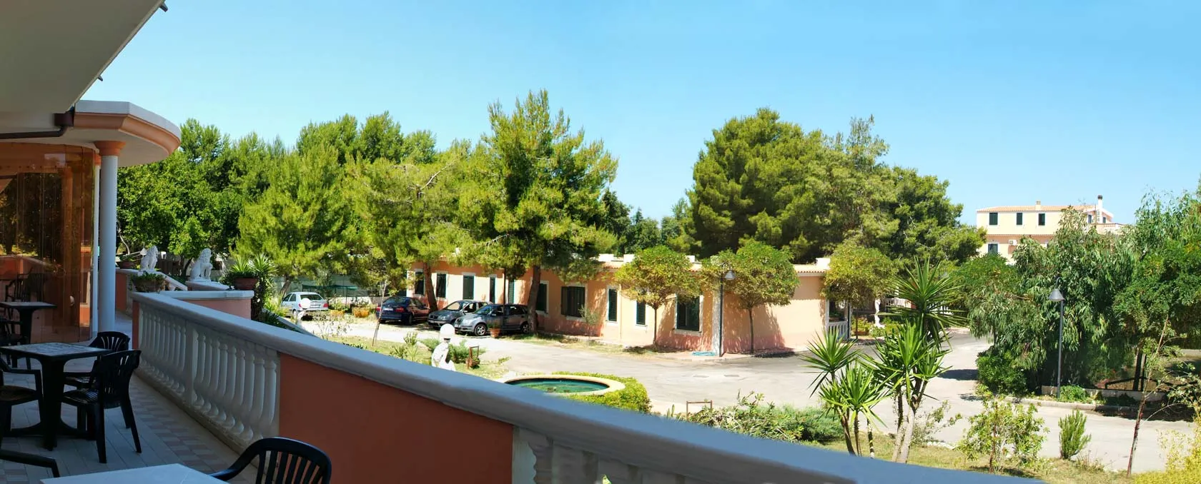 Vista dal balcone su giardino con pini, fontana e parcheggio dell'hotel