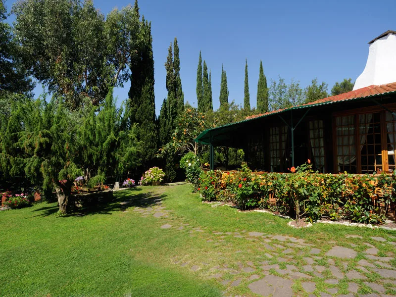 Giardino verde con prato, cipressi e veranda coperta con fiori colorati