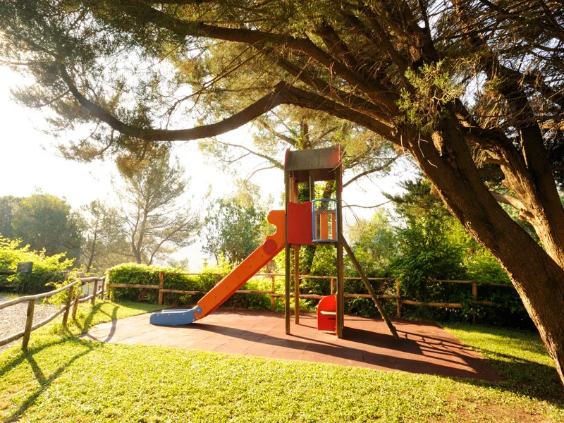 Area giochi per bambini con scivolo in un giardino alberato