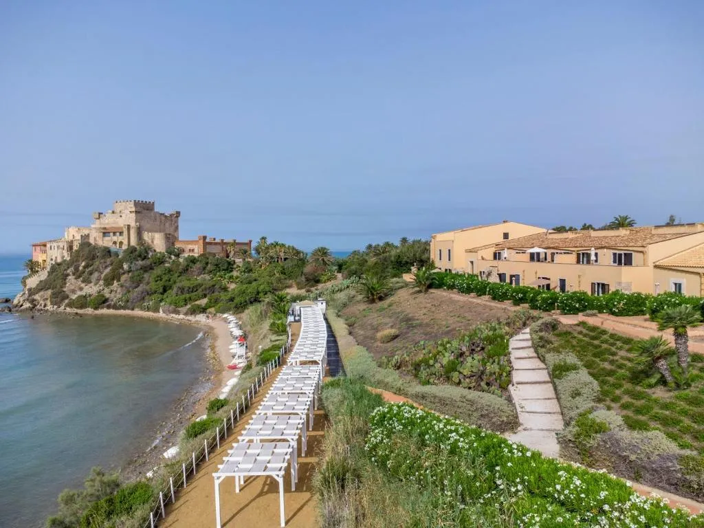 Vista della costa con castello sul promontorio, spiaggia con pergole bianche e giardini
