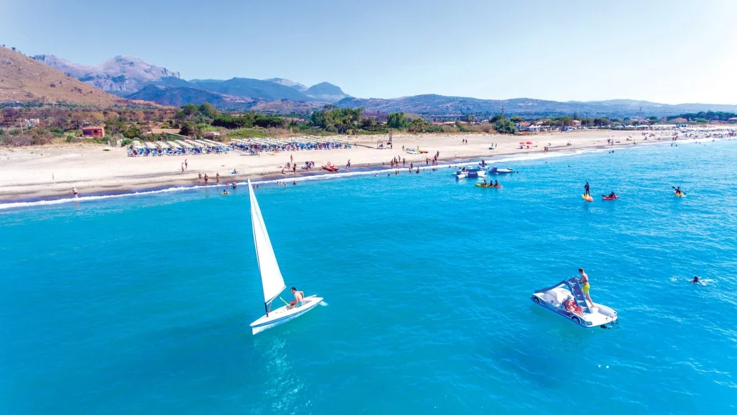 Mare cristallino con barca a vela e pedalò davanti alla spiaggia