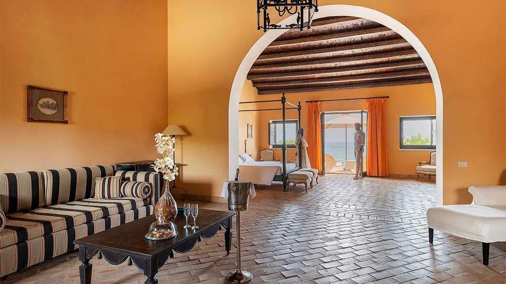Soggiorno della suite con divano a righe, arco in muratura e camera con vista mare