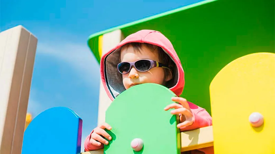 Bambino con occhiali da sole gioca su una struttura colorata del parco giochi