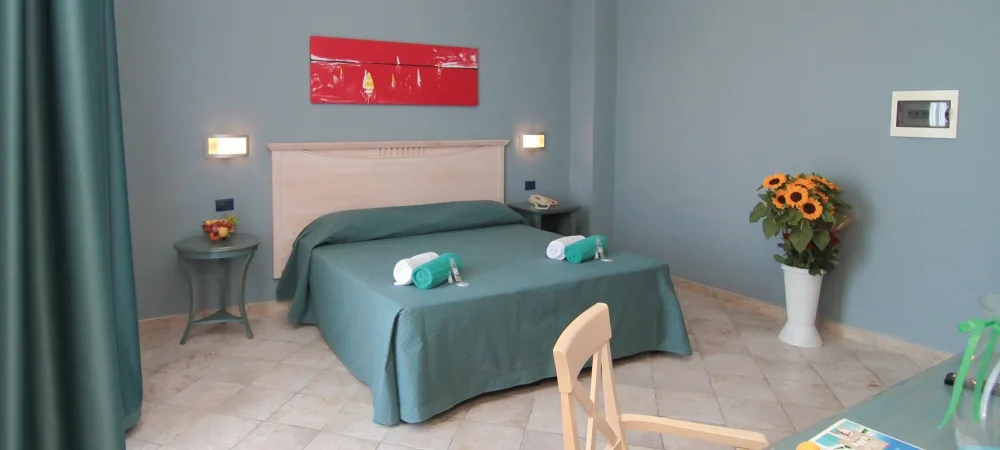 Camera matrimoniale con pareti azzurre, letto con copriletto verde, comodini e quadro rosso decorativo