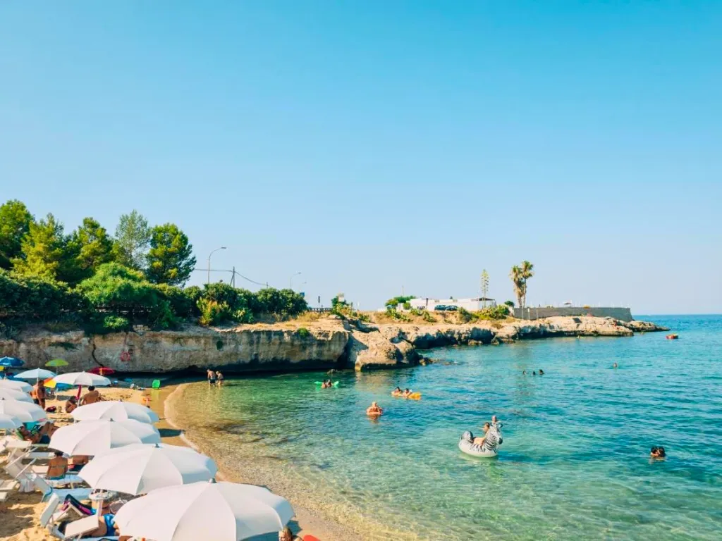 Cala con acqua cristallina, bagnanti e ombrelloni bianchi sulla spiaggia