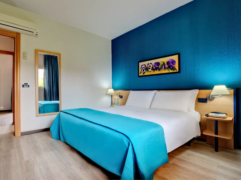 Camera matrimoniale con parete blu, letto con copriletto azzurro e specchio