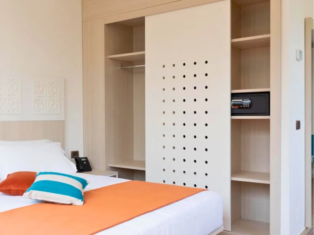 Dettaglio camera con letto, cuscini decorativi e guardaroba con cassaforte