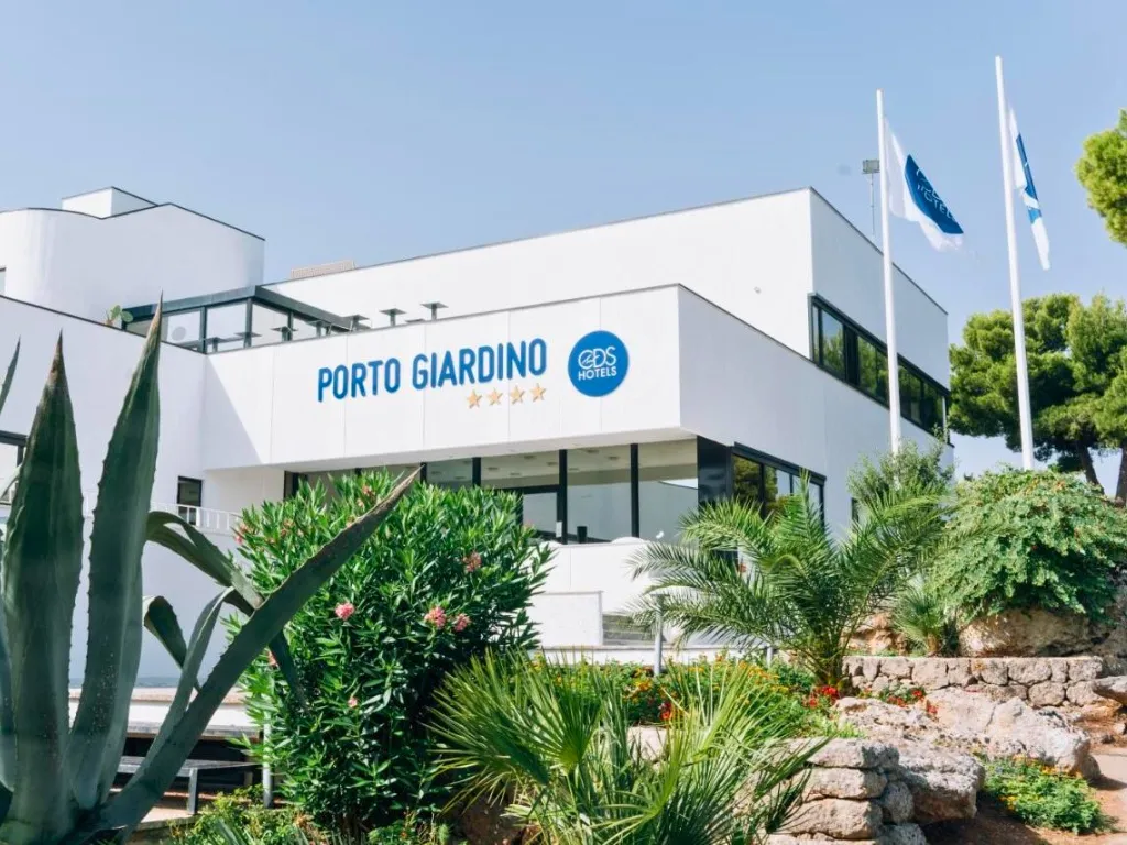 Ingresso dell'hotel Porto Giardino con insegna, edificio bianco e vegetazione mediterranea