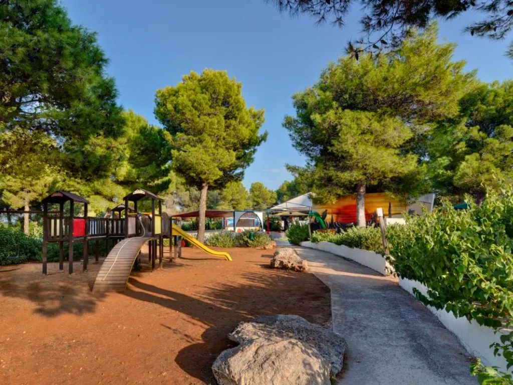 Parco giochi per bambini con scivoli e strutture in legno tra alberi ombrosi
