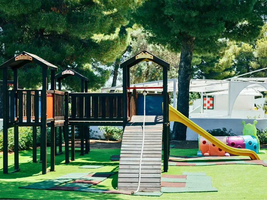 Area giochi per bambini con scivoli colorati e struttura in legno su prato sintetico