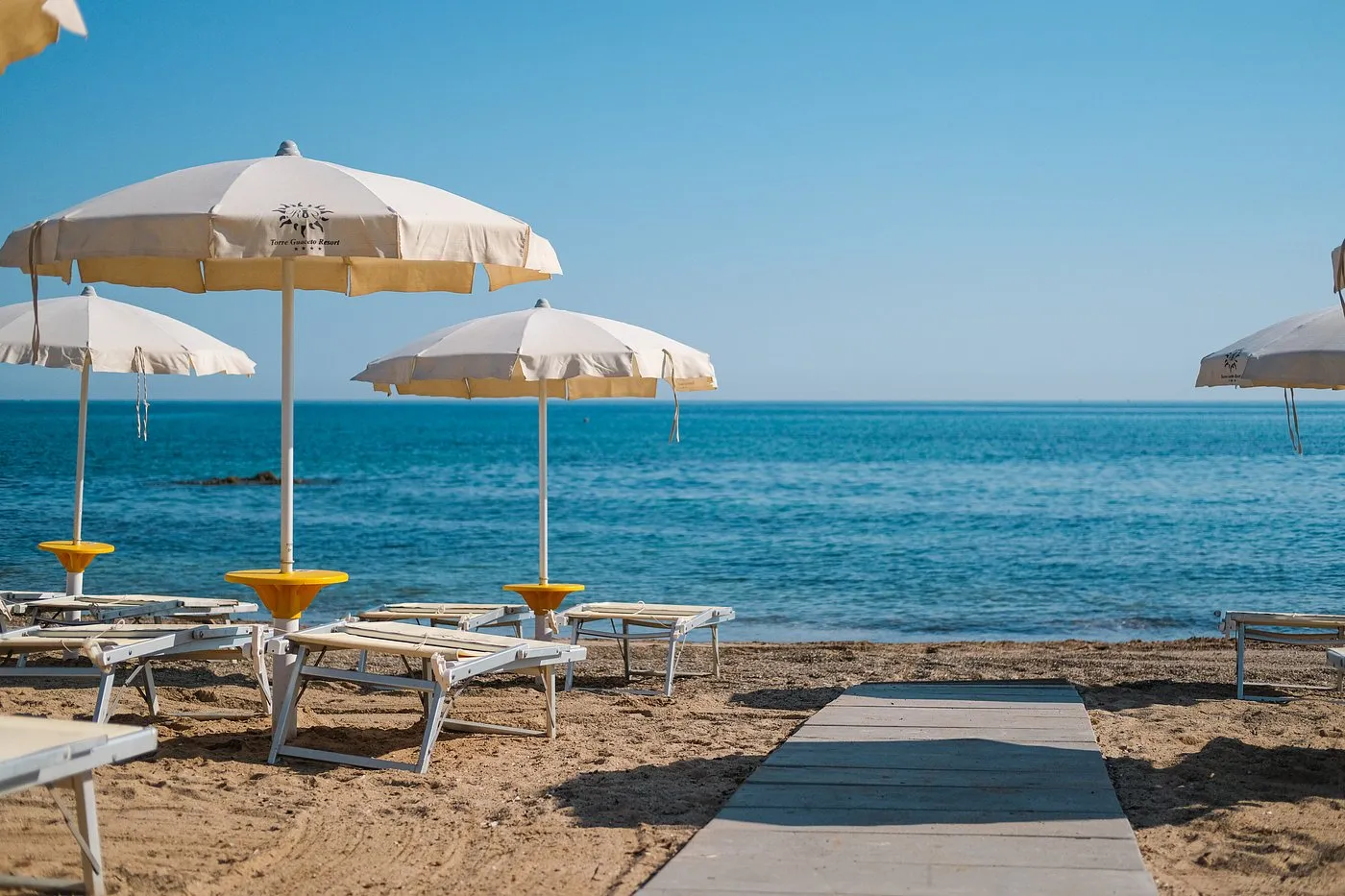 Ombrelloni e lettini in spiaggia con passerella in legno verso il mare