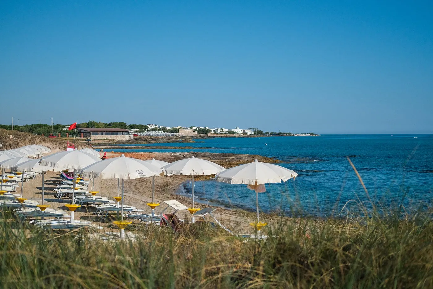 Costa con ombrelloni bianchi lungo la spiaggia e mare azzurro
