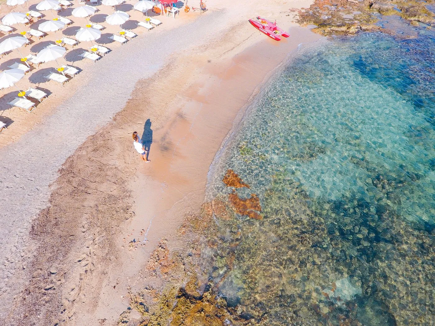 Spiaggia con ombrelloni, coppia in riva al mare e acqua cristallina