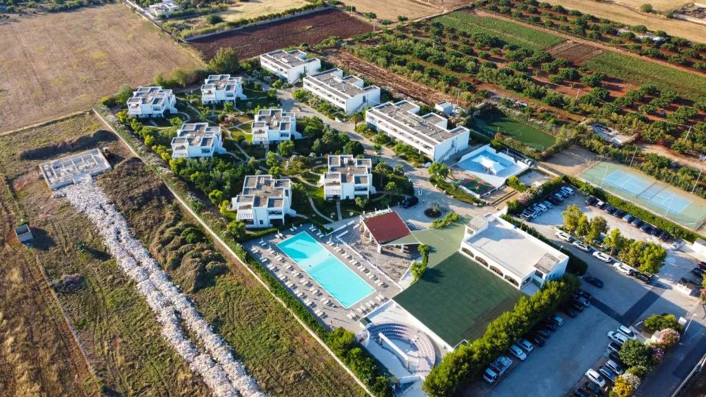 Vista aerea del resort con ville bianche, piscina, campi sportivi e parcheggio