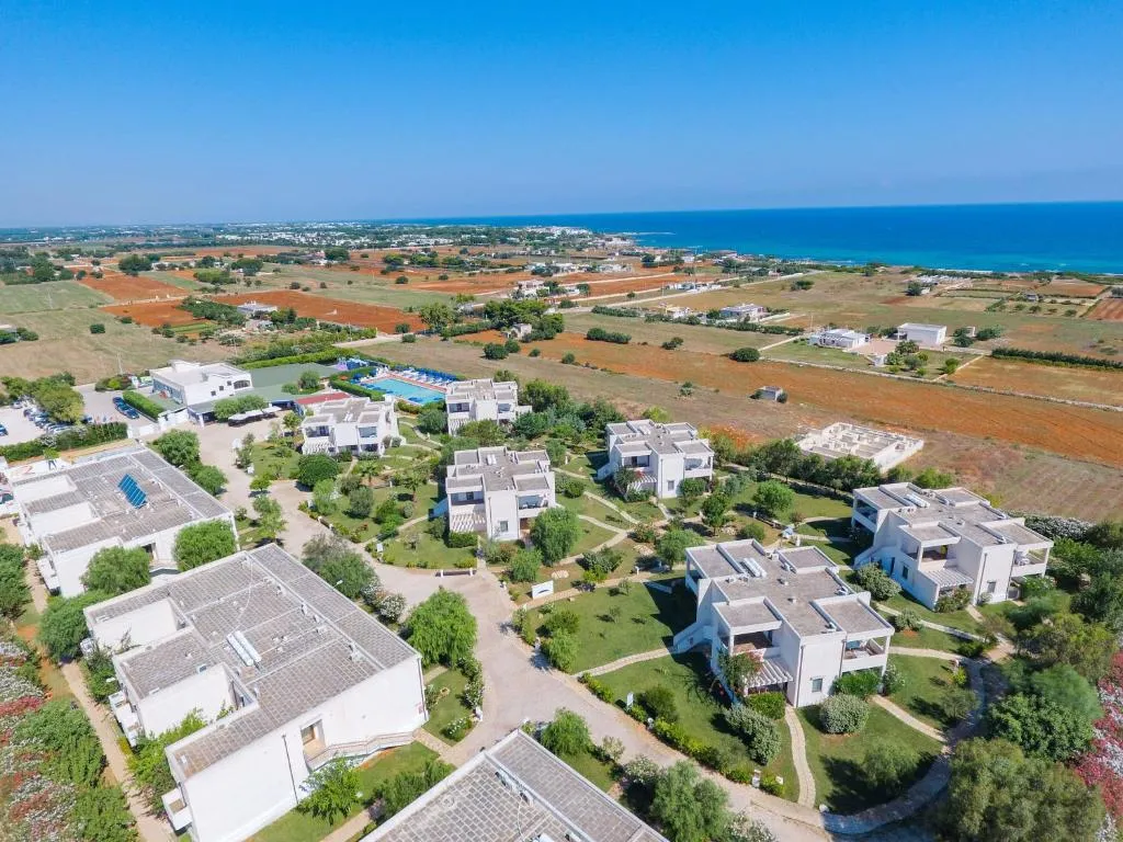 Vista aerea del complesso residenziale con giardini, ville bianche e mare sullo sfondo