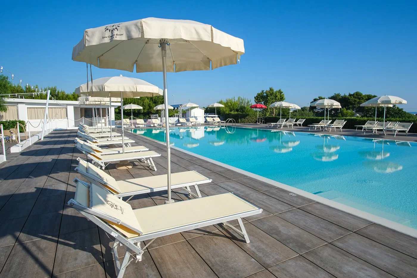 Piscina con pavimentazione in legno, lettini e ombrelloni del Torre Guaceto Resort