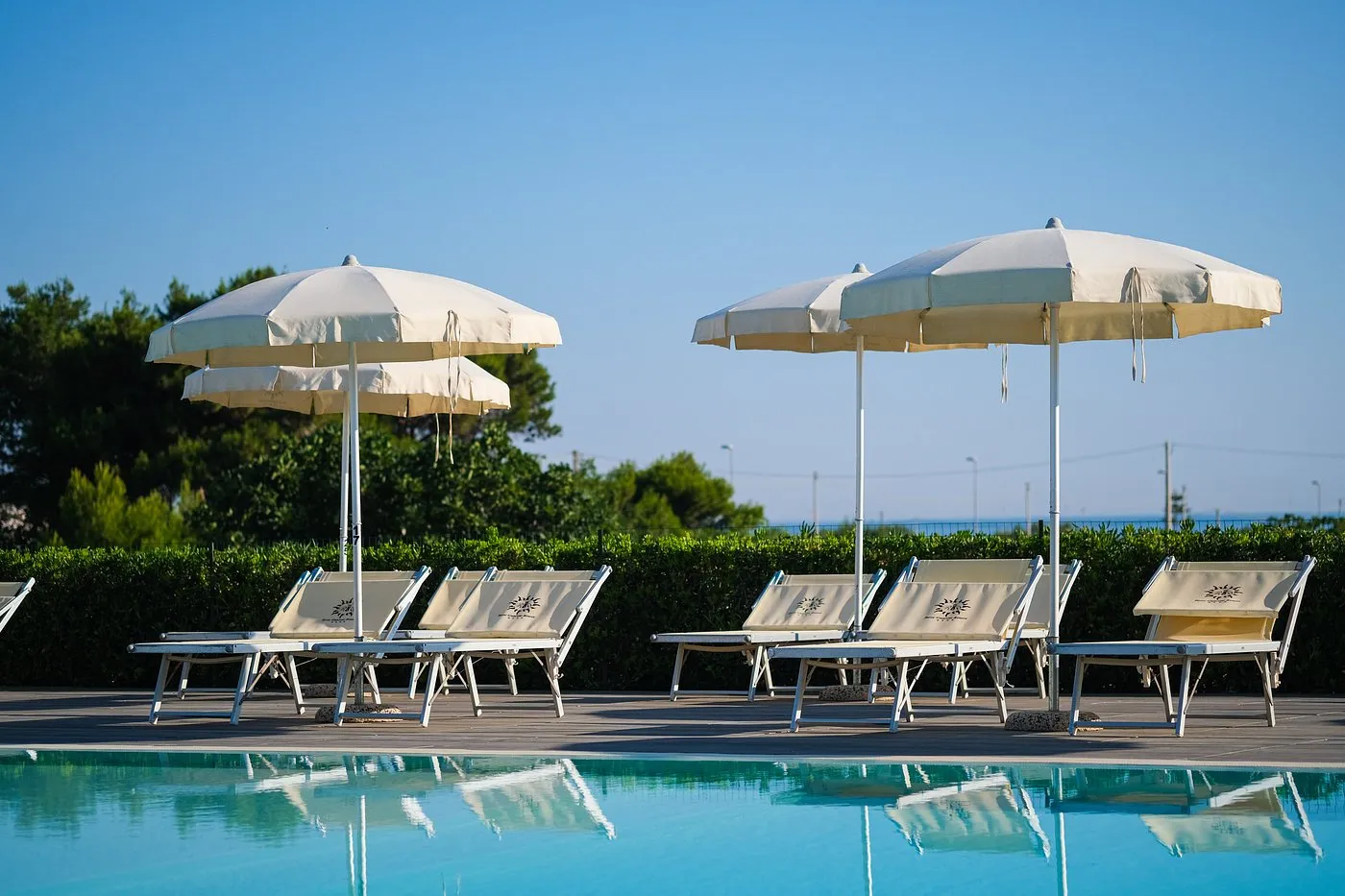 Lettini e ombrelloni bianchi a bordo piscina con cielo azzurro