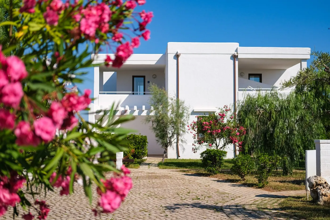 Villa bianca del resort con balcone e oleandri rosa in primo piano