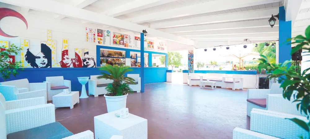 Bar lounge con arredi bianchi in vimini e pareti blu decorate