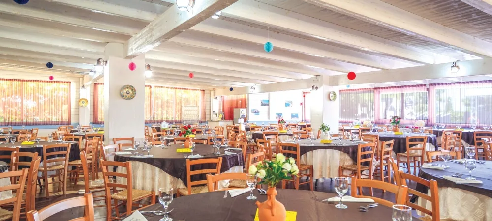 Sala ristorante interna con tavoli rotondi apparecchiati e sedie in legno