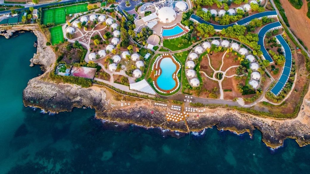 Vista aerea del resort su promontorio roccioso con bungalow a cupola, piscine e mare turchese