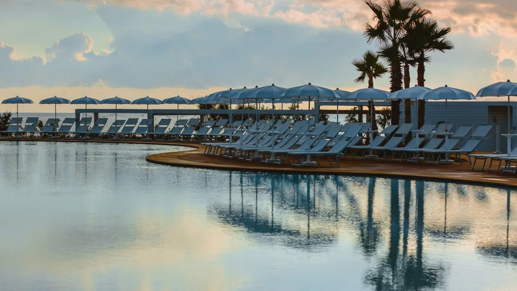 Piscina con lettini e ombrelloni azzurri riflessi nell'acqua al tramonto
