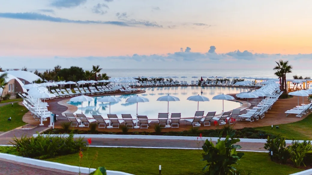 Piscina circolare con ombrelloni e lettini vista mare all'alba