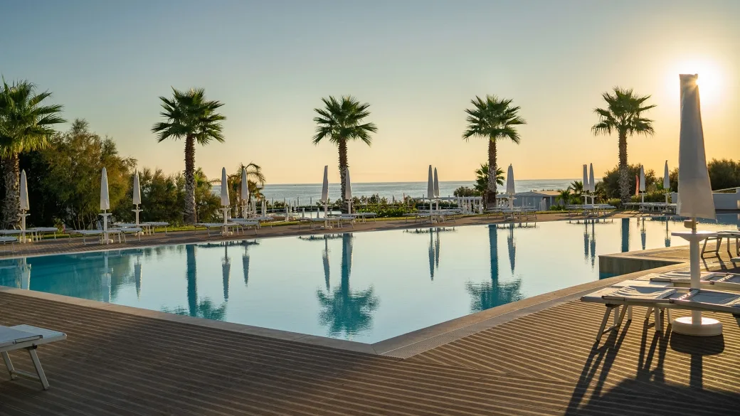 Piscina con palme e lettini vista mare durante il tramonto dorato