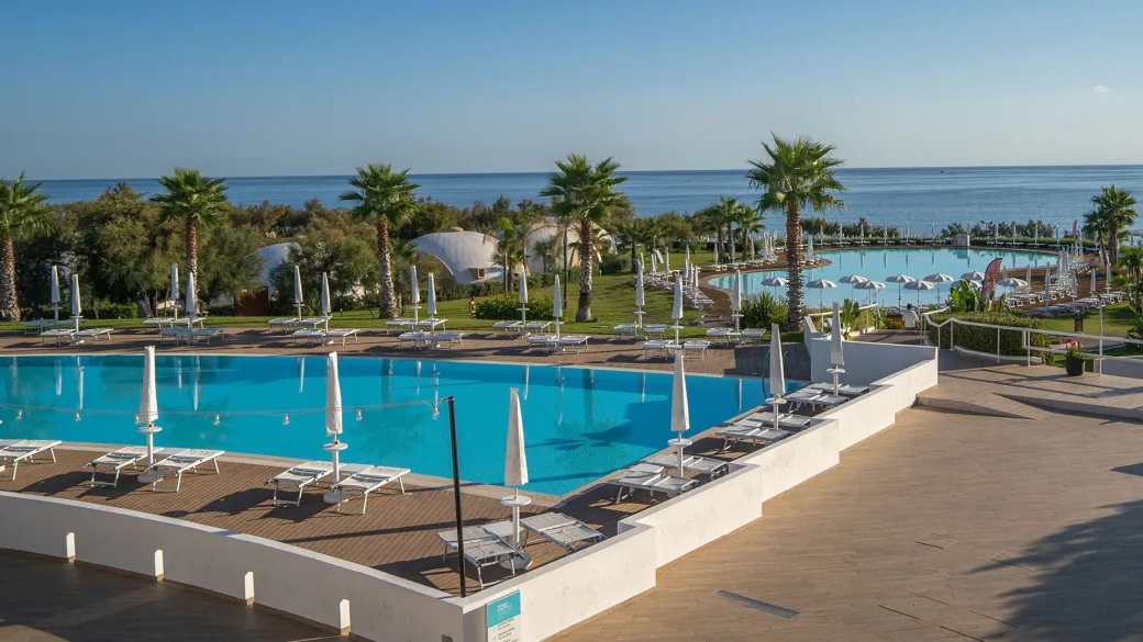 Vista panoramica di due piscine con lettini e palme affacciate sul mare
