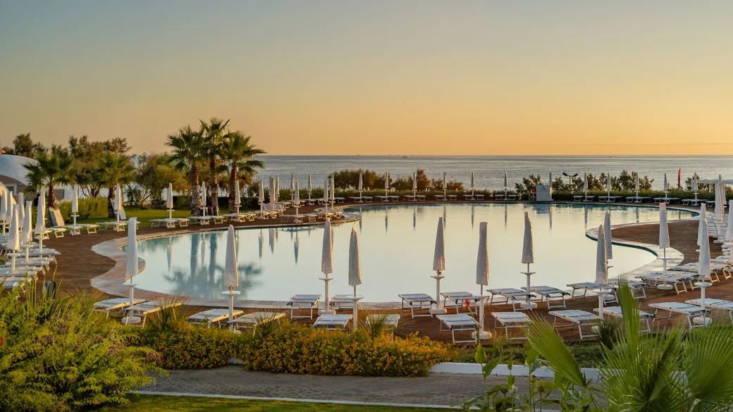 Piscina panoramica con lettini e palme affacciata sul mare al tramonto