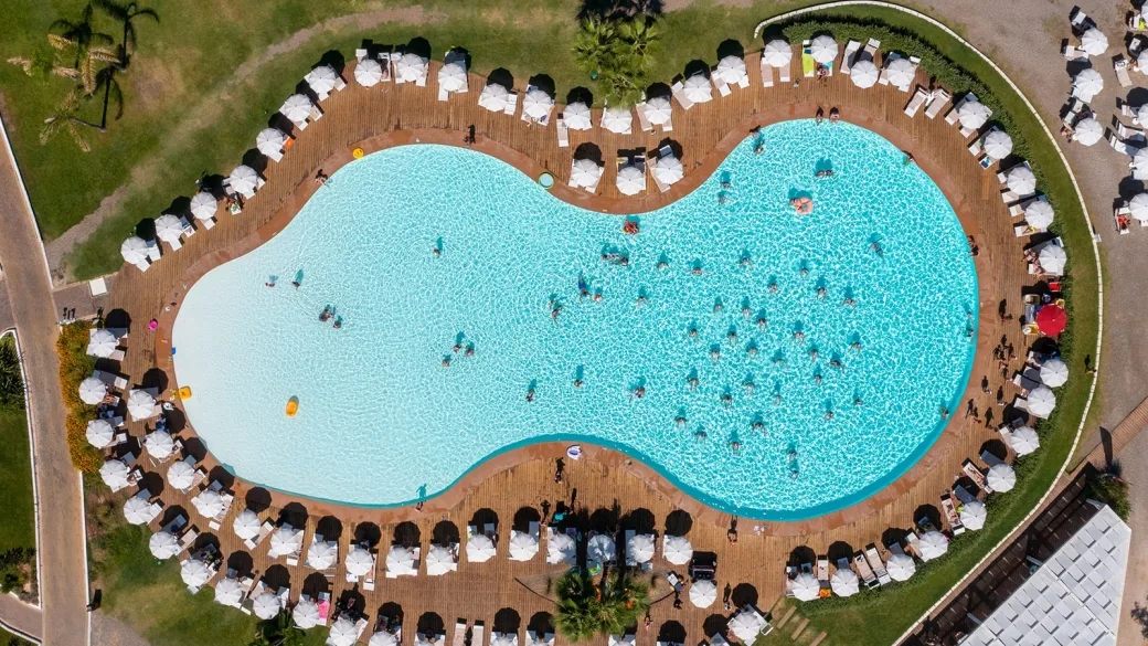 Vista aerea della piscina a forma sinuosa circondata da ombrelloni bianchi