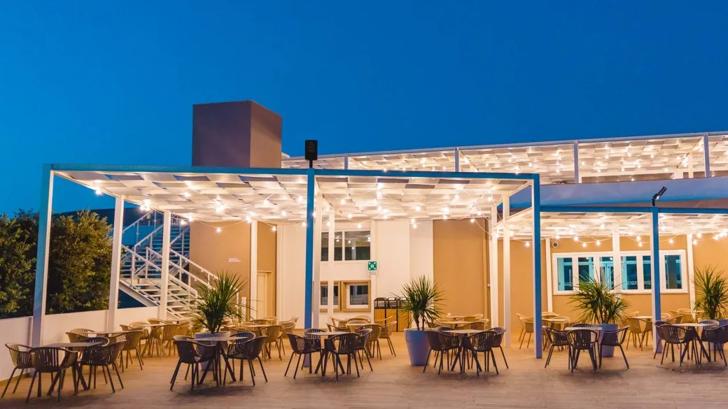 Terrazza esterna con tavoli e sedie sotto pergolato illuminato di sera