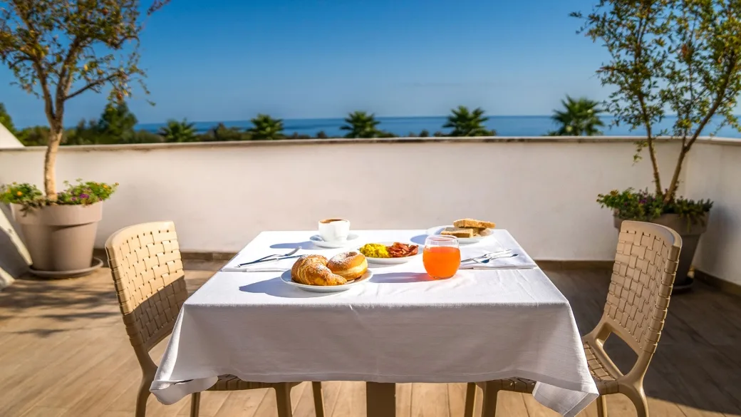 Colazione servita su terrazza con vista mare e piante in vaso