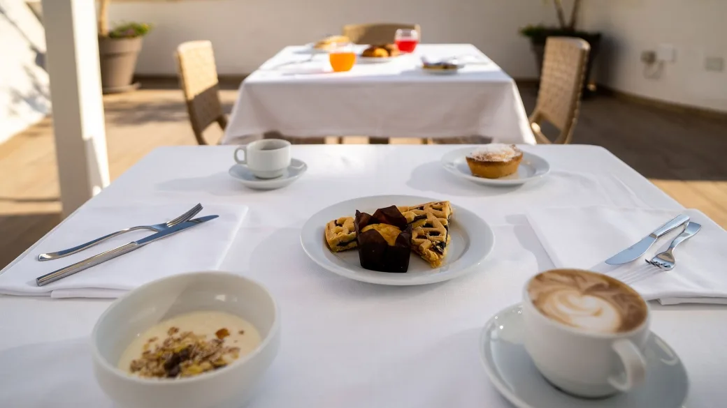 Tavolo apparecchiato per colazione con cappuccino, dolci e cereali all'aperto