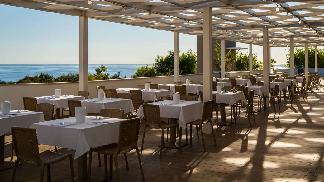 Ristorante su terrazza coperta con tavoli apparecchiati e vista sul mare