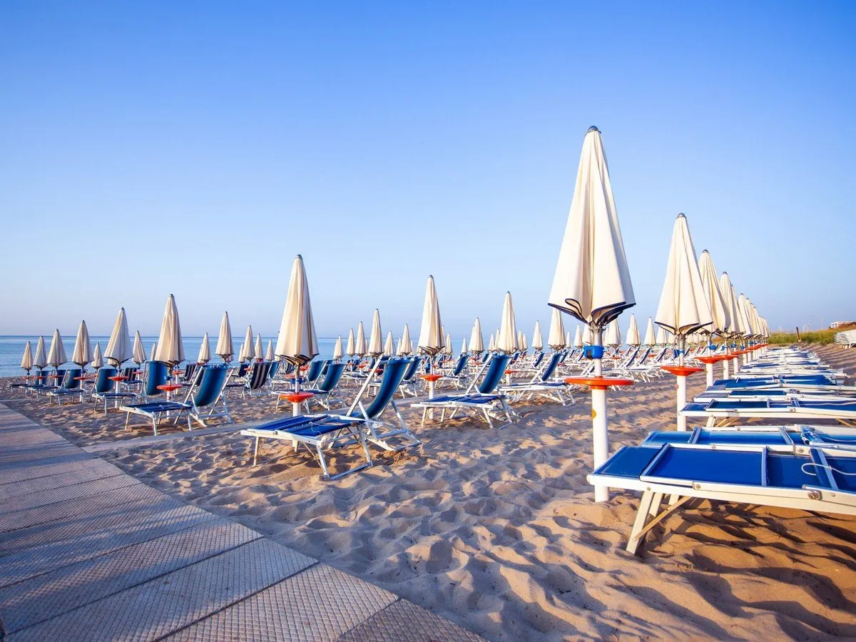File di ombrelloni e lettini sulla spiaggia sabbiosa con cielo sereno