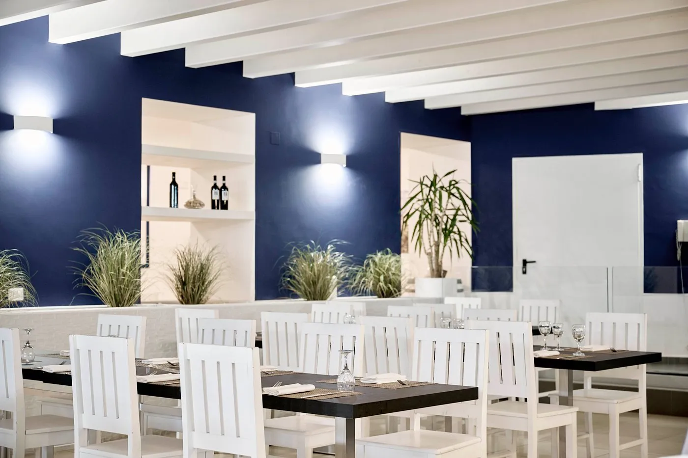 Sala ristorante con tavoli apparecchiati, sedie bianche e pareti blu
