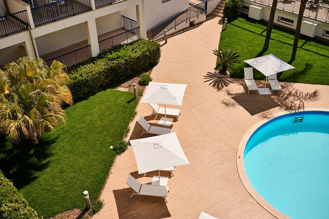 Vista dall'alto della piscina con lettini bianchi e giardino curato