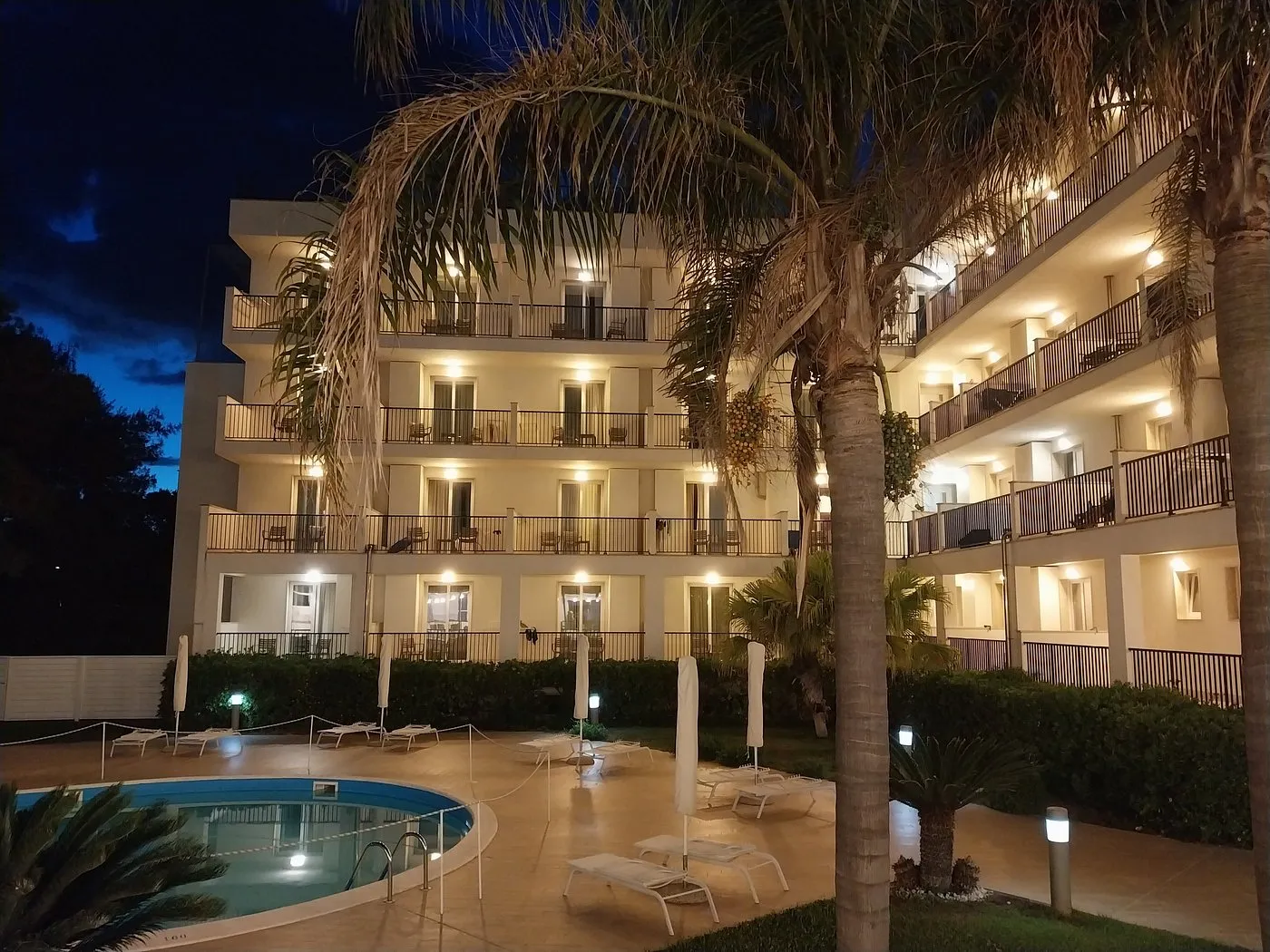 Esterno dell'hotel illuminato di sera con piscina e palme