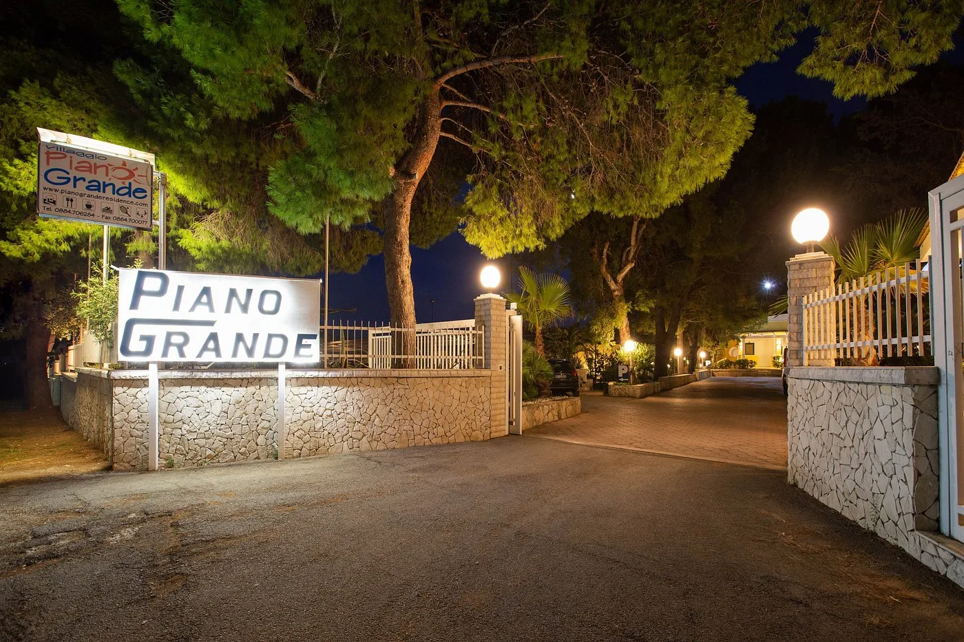 Ingresso notturno del villaggio Piano Grande con insegna illuminata e pini
