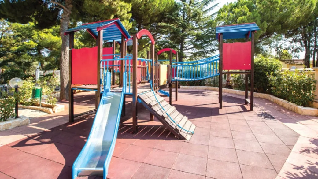 Area giochi per bambini con scivolo e struttura colorata all'ombra dei pini