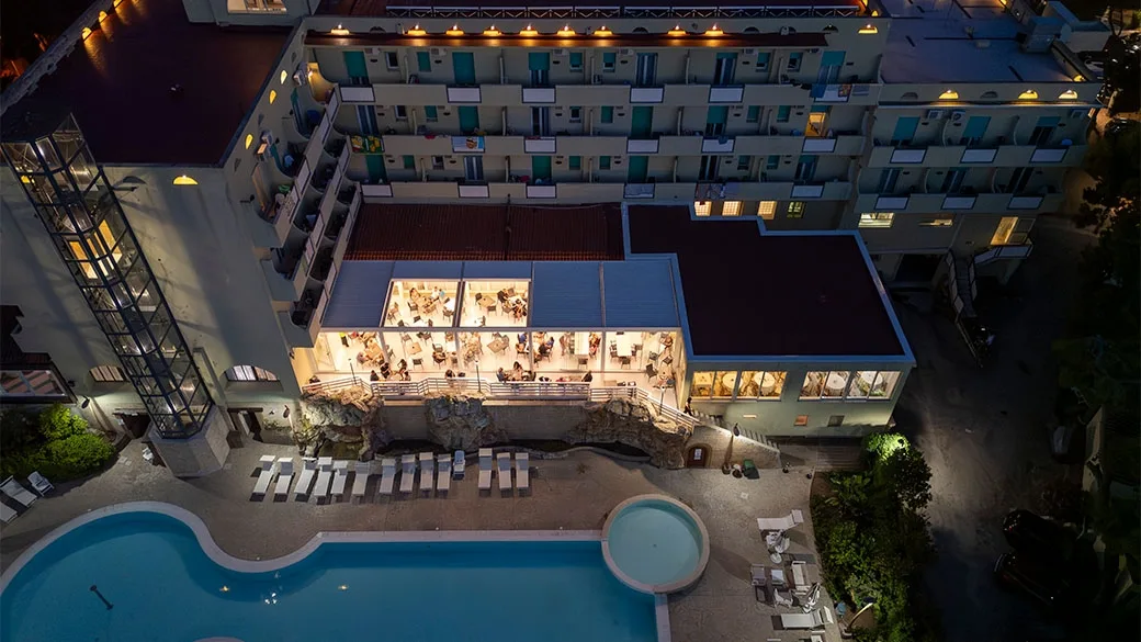Vista aerea notturna dell'hotel con piscina illuminata e sala ristorante