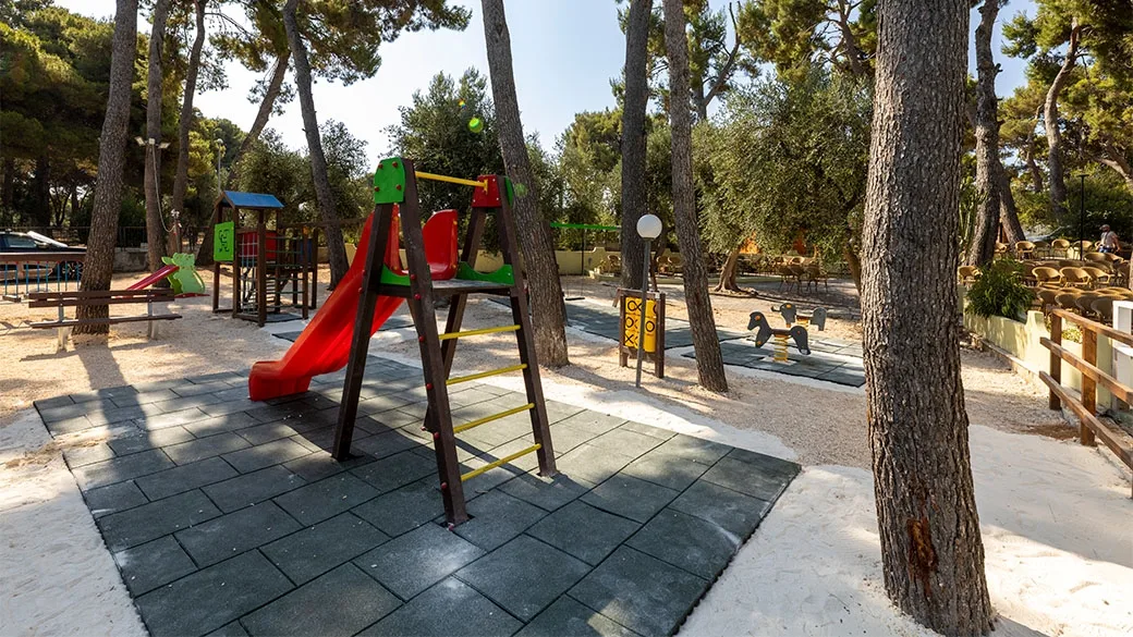Parco giochi per bambini con scivolo colorato all'ombra dei pini