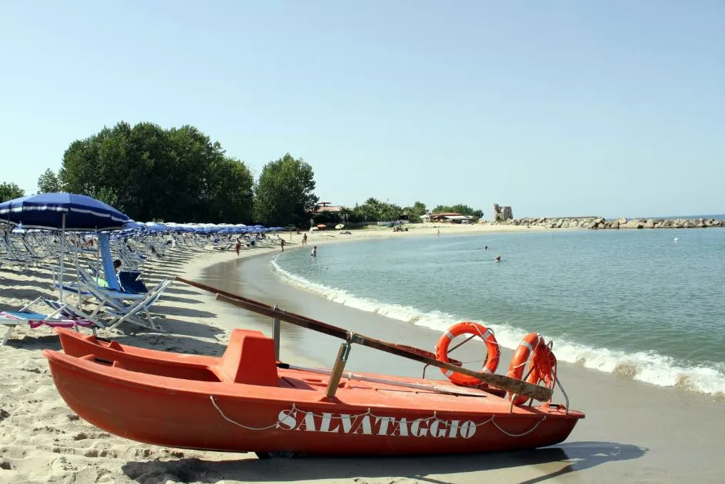 Spiaggia con barca di salvataggio arancione e ombrelloni blu lungo la riva