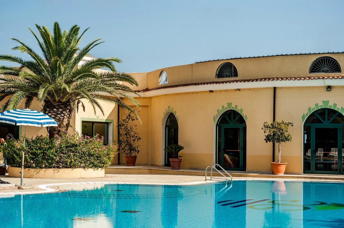 Edificio giallo del resort con archi verdi e palma a bordo piscina