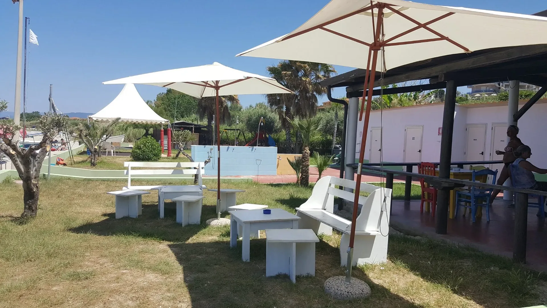 Area relax esterna con panche bianche, ombrelloni e area giochi per bambini