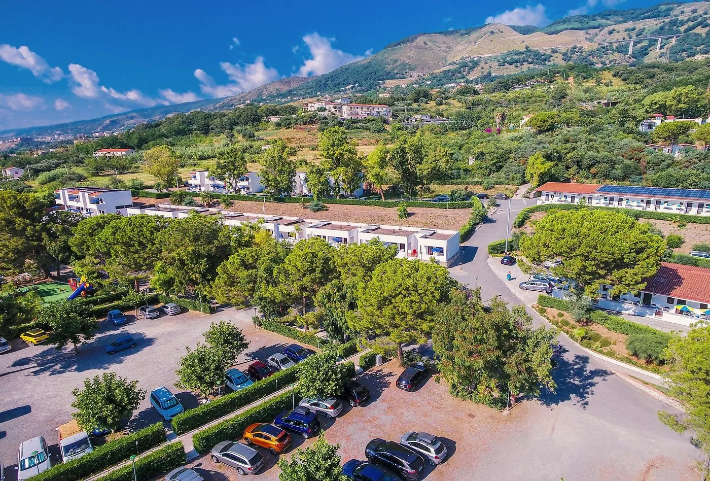 Veduta aerea delle villette bianche del resort tra alberi e parcheggio con colline